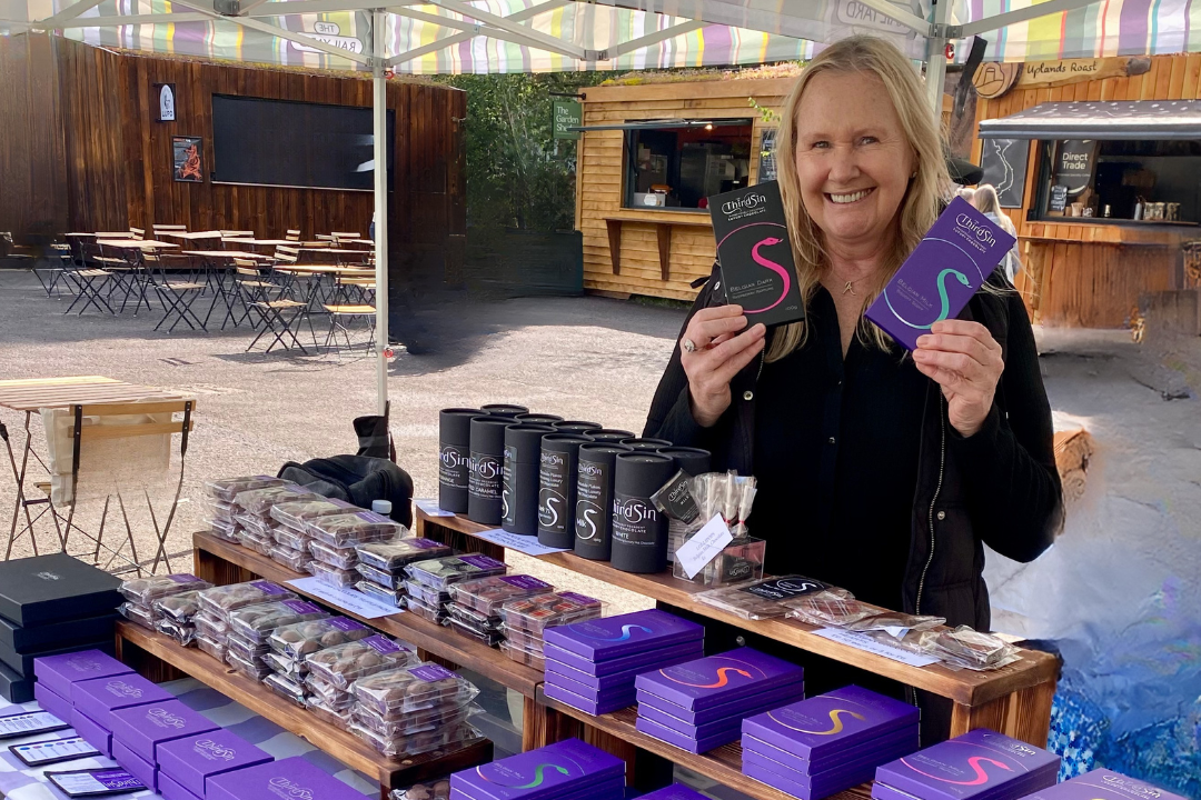 Woman holding purple boxes at a table with more boxes and products.
