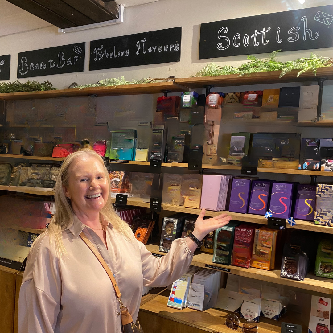 Woman standing in a store with shelves displaying various products and signs indicating 'Scottish' and 'Flavours'.
