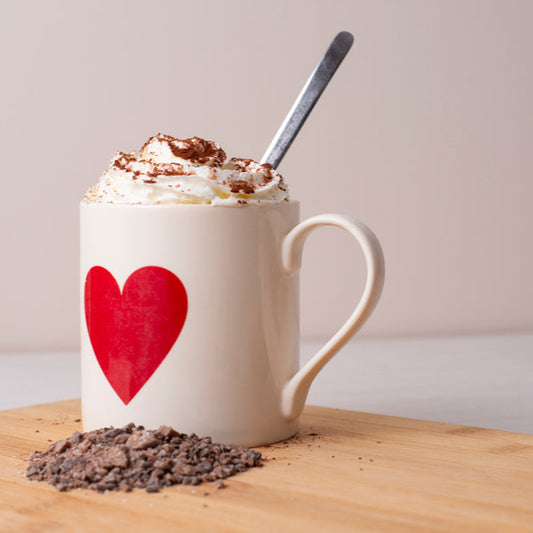 White mug with red heart design filled with hot chocolate on a wooden surface.