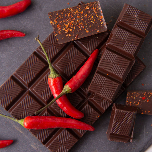 Dark chocolate bars with red chili peppers on a dark surface