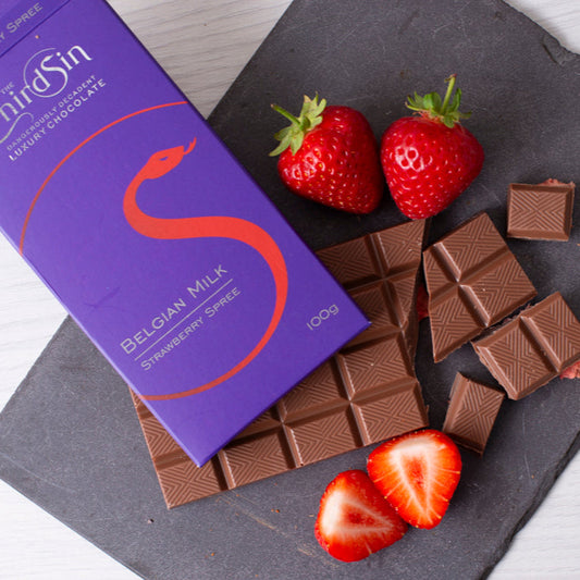 Chocolate bars with strawberries on a slate surface, featuring 'The Third Sin' brand.