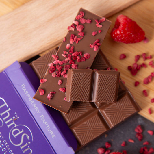 Chocolate bars with raspberry pieces on a wooden board, featuring the Third Sin brand.