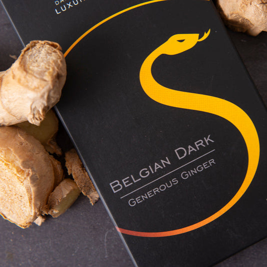 Black packaging with yellow snake design labeled 'Belgian Dark Generous Ginger' on a dark surface with ginger roots.