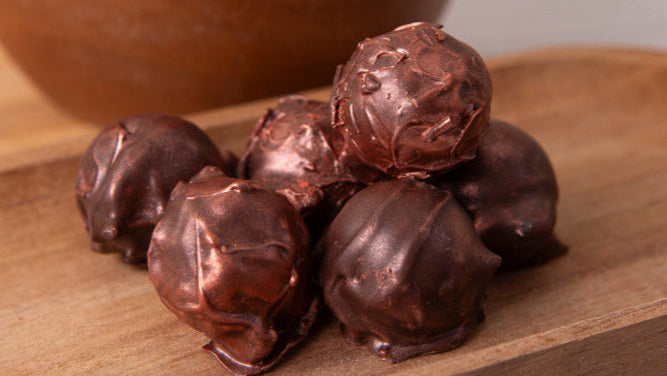 Chocolate truffles on a wooden board with a wooden bowl in the background