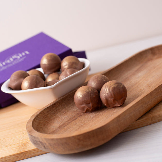 Wooden tray with chocolate truffles and a purple box on a white surface