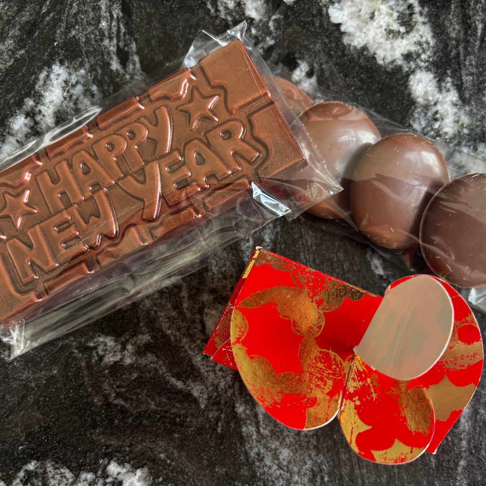 Chocolate bar with 'Happy New Year' text, wrapped chocolates, and a red envelope on a dark surface.