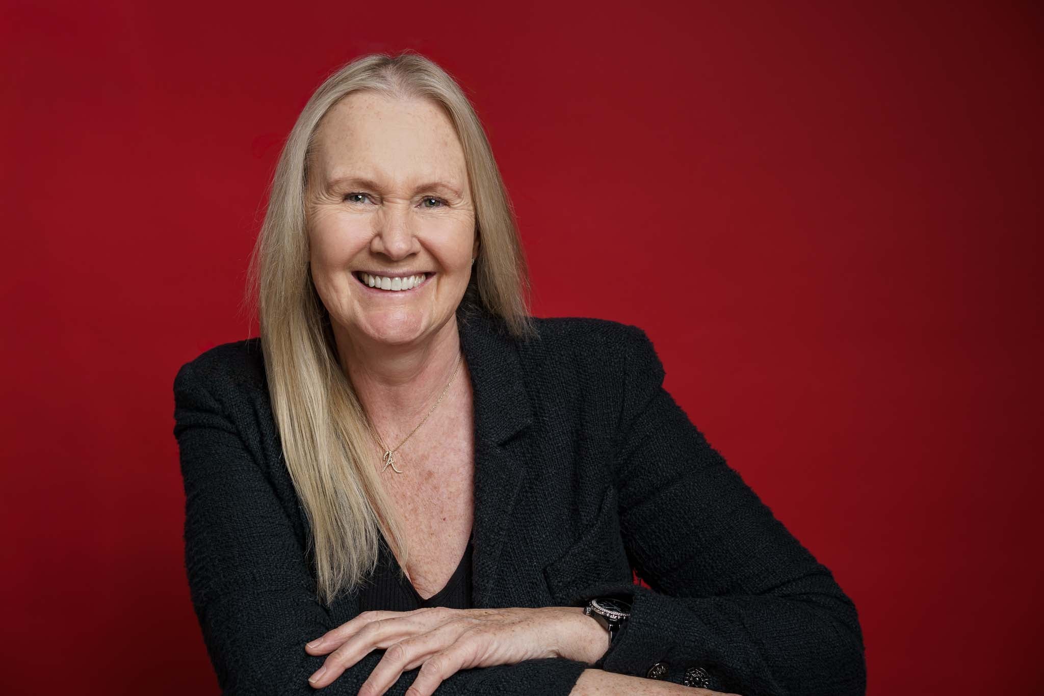 Ann in a black jacket smiling against a red background