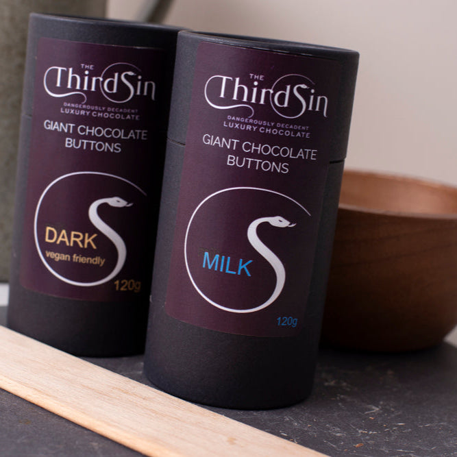 Two bottles of Third Sin Giant Chocolate Buttons on a surface with a bowl and wooden stick in the background.