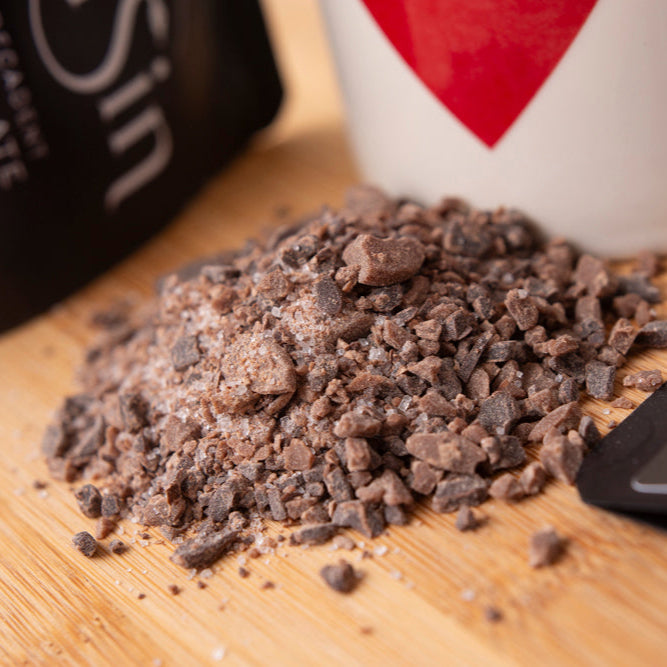 Cocoa powder on a wooden surface with a cup and chocolate packaging in the background.