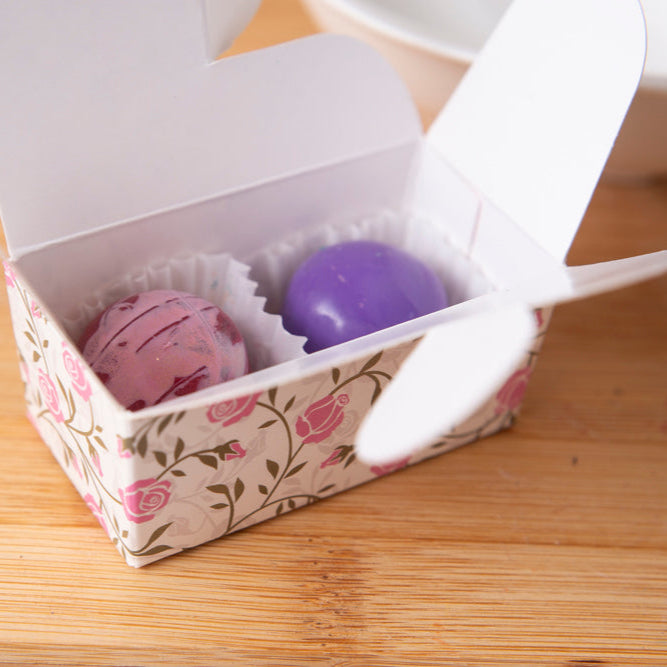 Two purple bath bombs in a decorative box on a wooden surface
