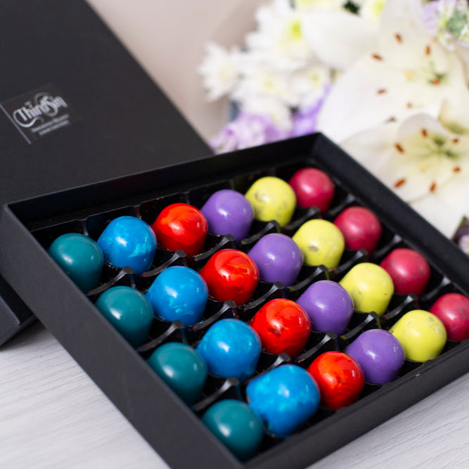 Assorted colorful candies in a black box with a floral arrangement in the background.