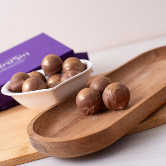 Wooden tray with chocolate truffles and a purple box on a white surface