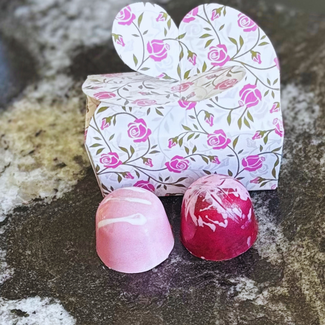 Heart-shaped floral box with two pink marbled chocolates on a textured surface
